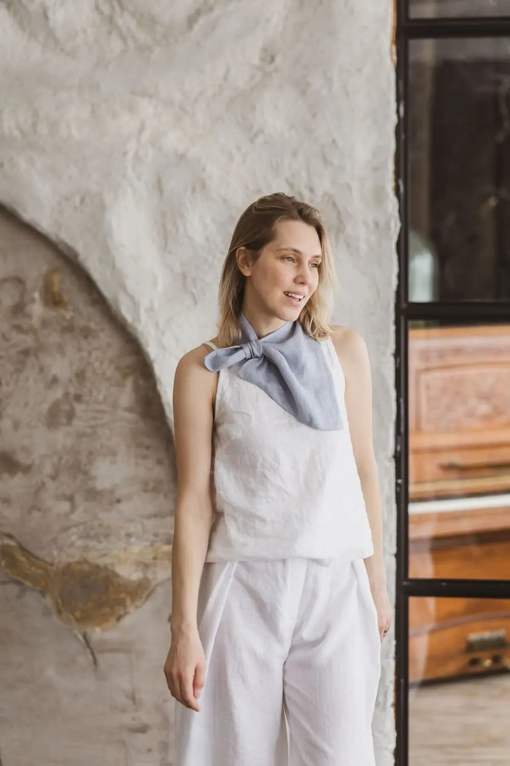 Woman wearing light blue linen neckerchief with pre-stitched loop over white linen outfit