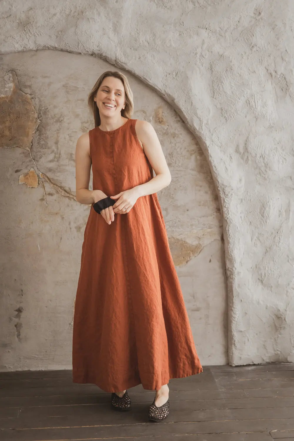 Woman smiling in a sleeveless rust linen maxi dress with A-line silhouette, full length front view