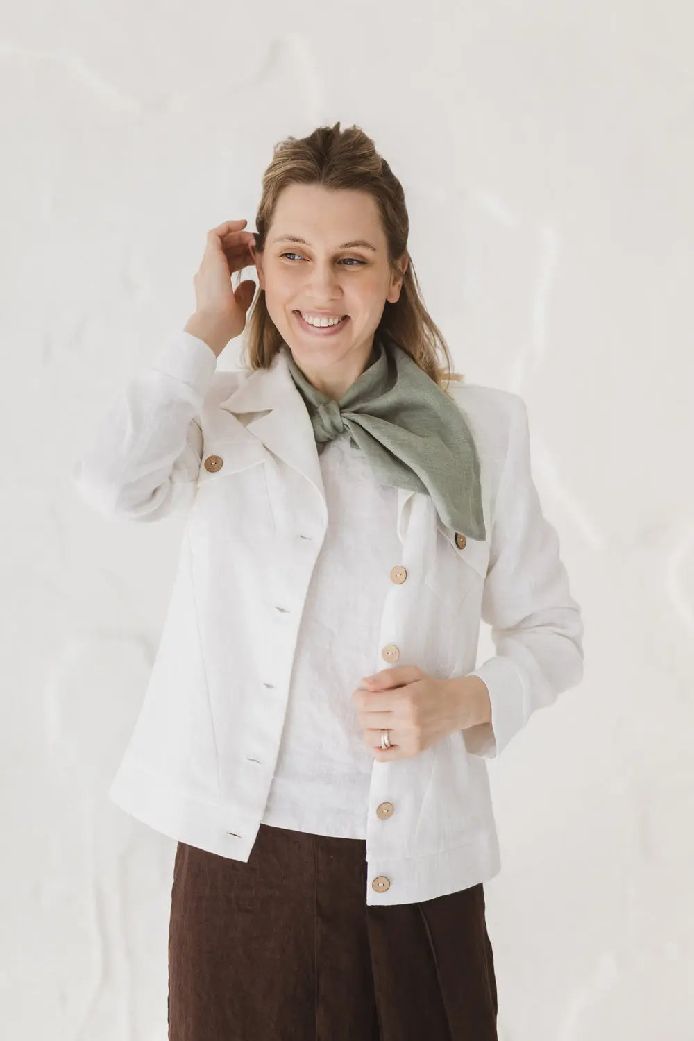 Woman wearing a light green linen gauze linen scarf with a white jacket