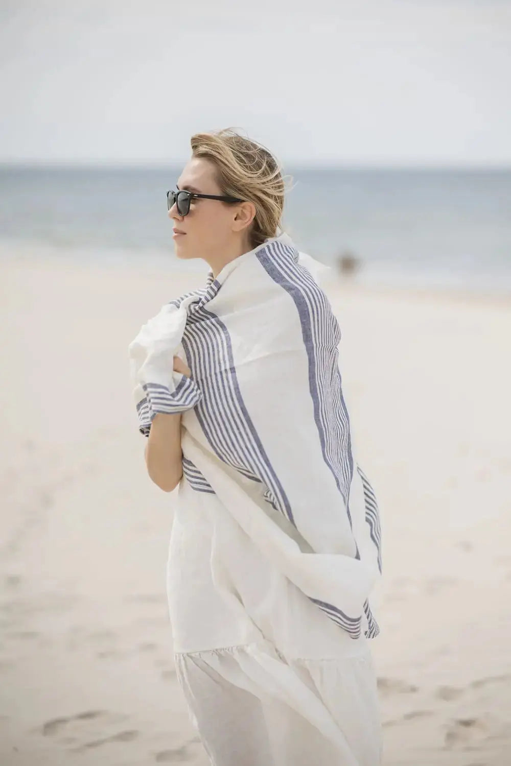Side view of a woman wrapping herself in a soft blue striped linen beach towel