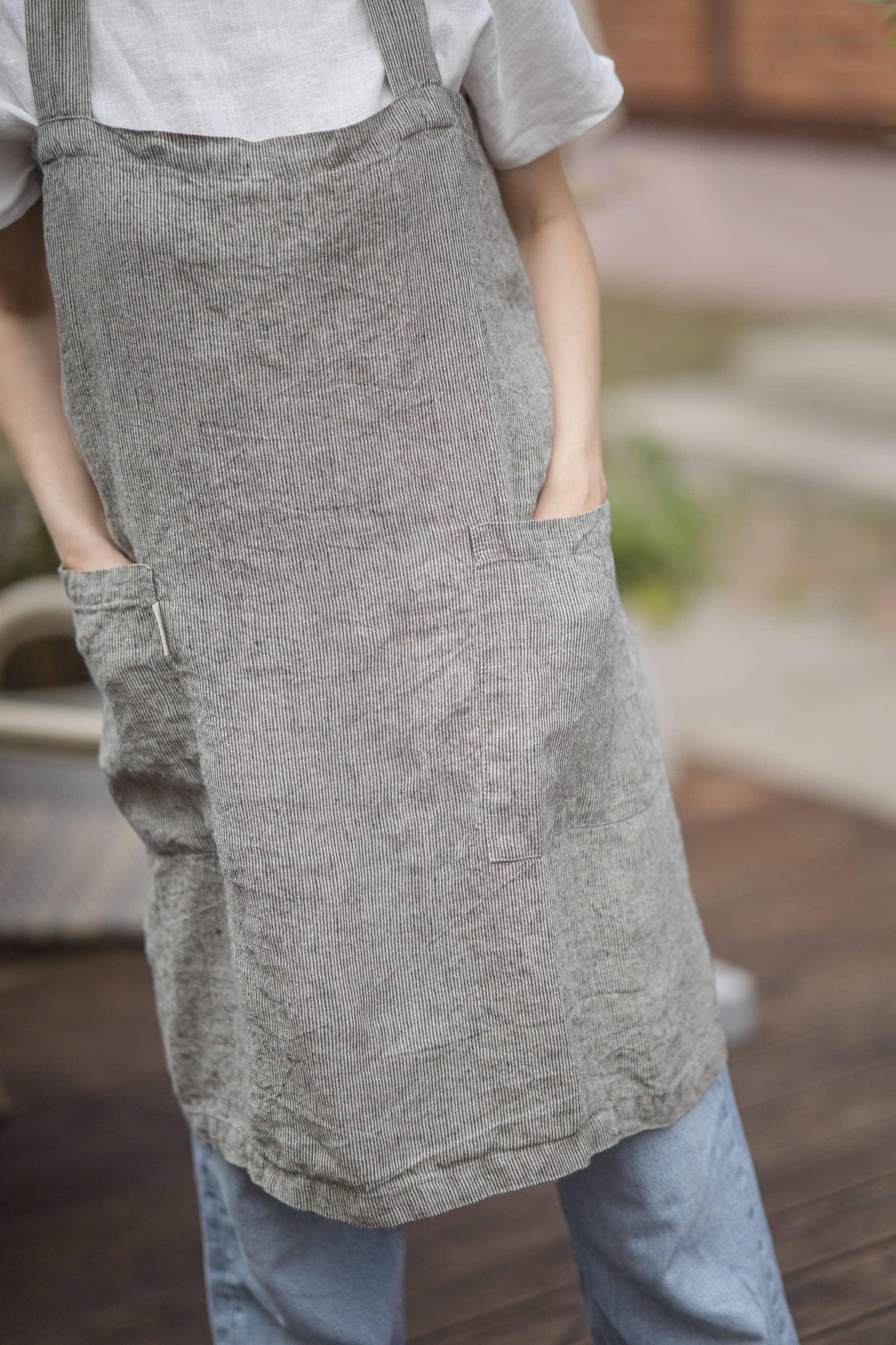 Close-up of the grey striped linen apron's front pockets, hands tucked inside the pockets.