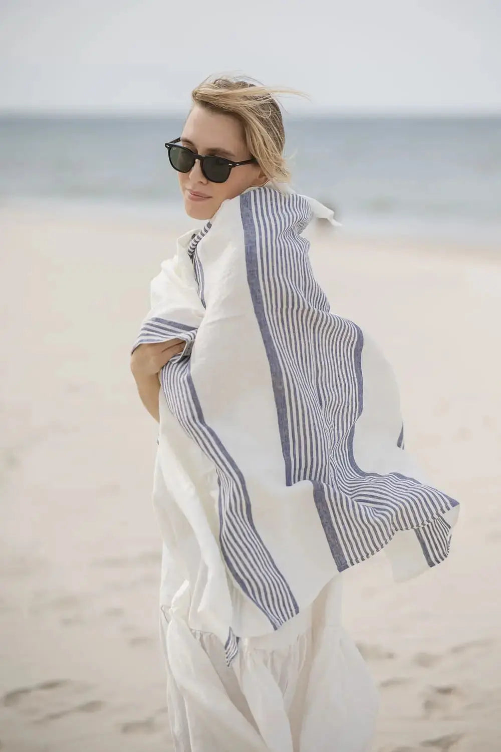 Portrait of a woman holding a white and blue striped linen towel on the beach