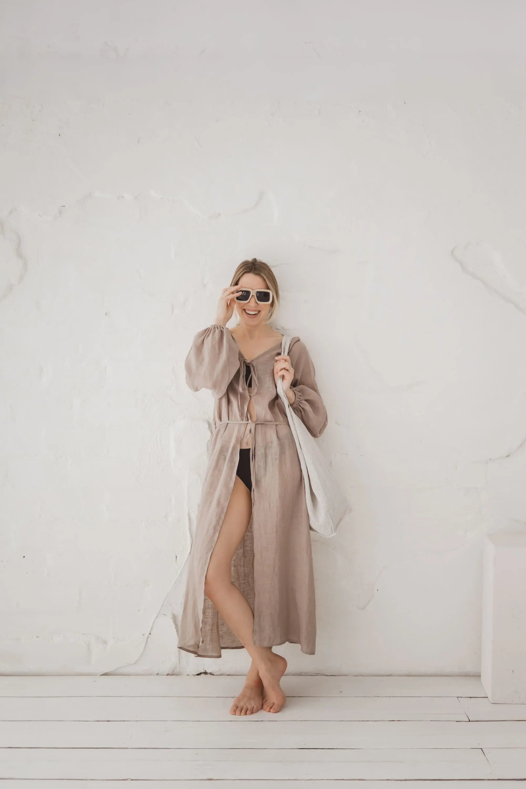 Woman wearing a flowing natural linen kaftan with long sleeves and waist tie, full length front view