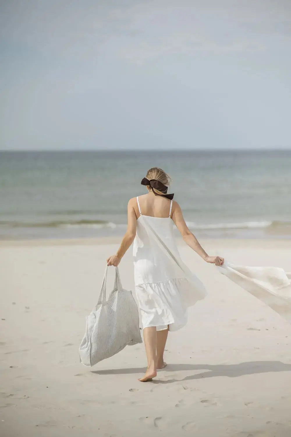 Woman carrying Linen Huckaback Beach Towel in white natural striped, walking on the beach