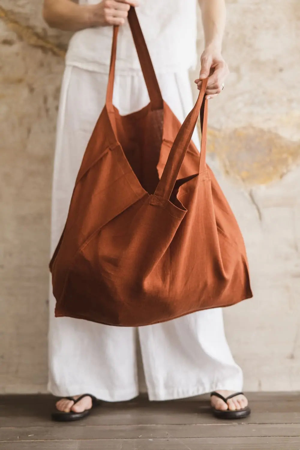 Large terracotta linen tote bag held with both handles showing spacious soft silhouette
